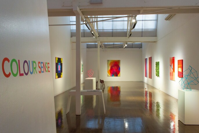 Interior of Arc One Gallery displaying bright artworks hanging on a white wall.