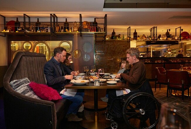 Four people eating at a restaurant, two are sitting in wheelchairs.