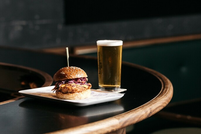 A hamburger and glass of beer on a rounded bar.