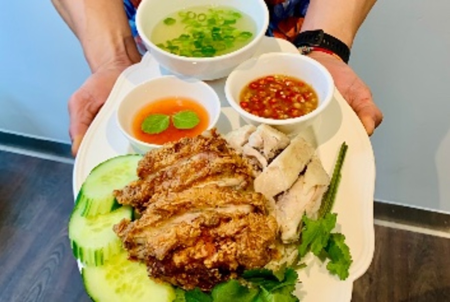 Pair of hands holding a large plate of cooked chicken over rice and salad with bowls of sauces of the side.