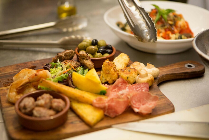 Tongs hovering over a charcuterie platter with olives, meat and bread.