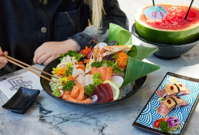 A black bowl filled with sashimi at a restaurant and a watermelon cocktail.