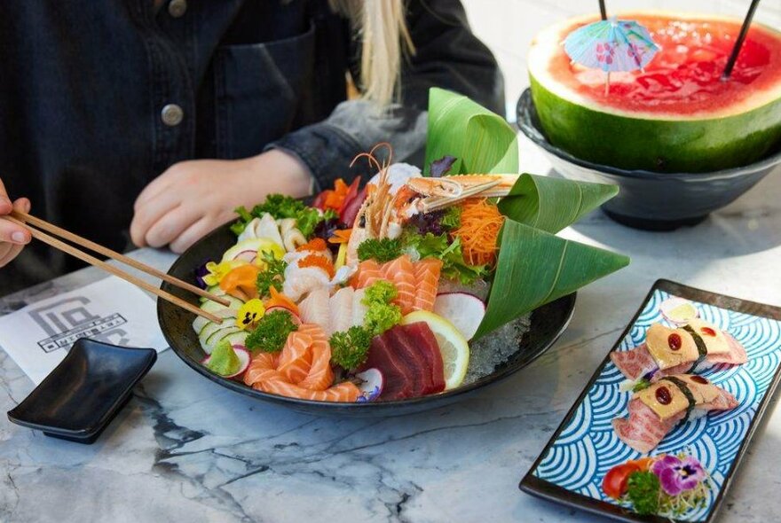 A black bowl filled with sashimi at a restaurant and a watermelon cocktail.