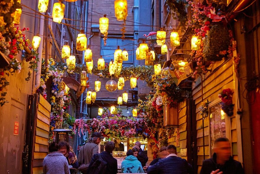 People sitting in a narrow bar under lanterns.