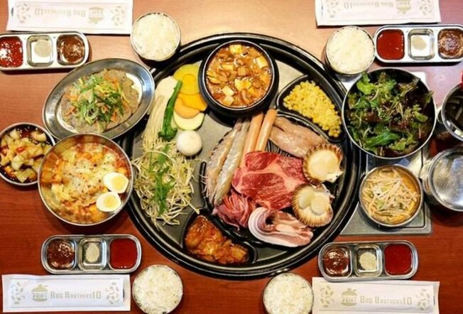 A hot plate with meat and vegetables on it surrounded by side dishes.