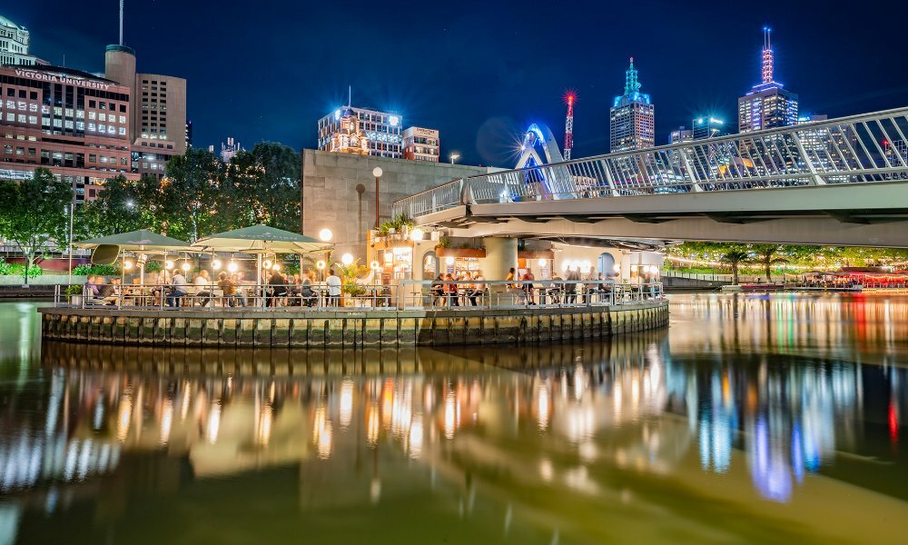 A busy floating bar on the river at night with the city skyline lights in the background.