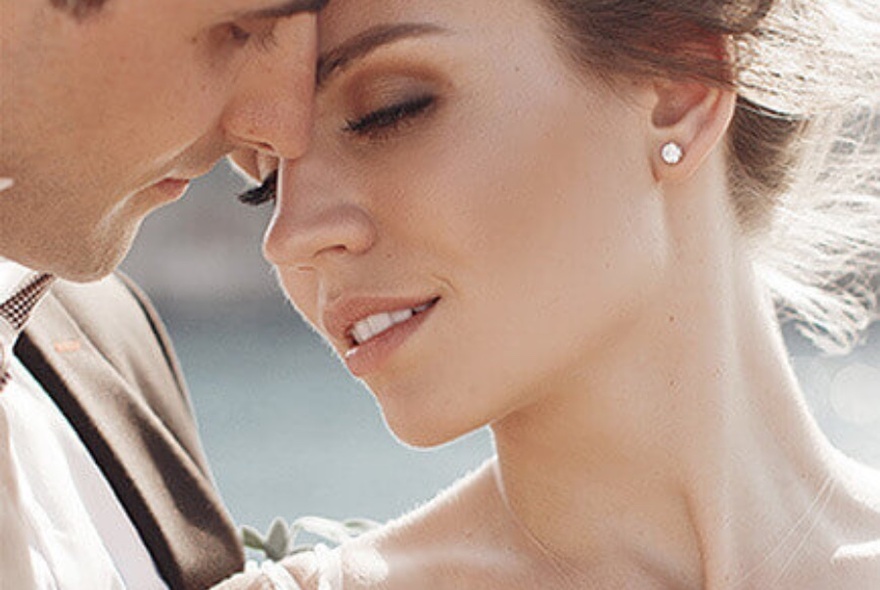 A close up of a bride and groom. The bride is wearing diamond earrings. 