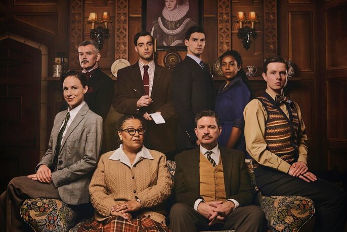 The cast of Agatha Christie's The Mousetrap, all assembled in dimly lit room around a patterned sofa. 