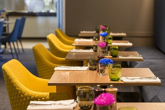 Empty tables set for dinner with a yellow chair at each table.