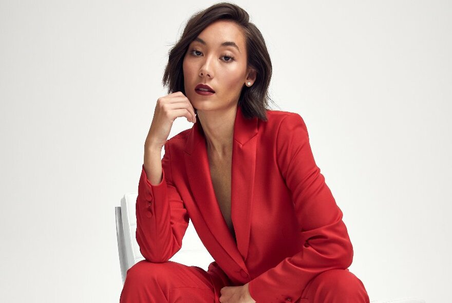 A model in a seated pose wearing a low cut red suit. 