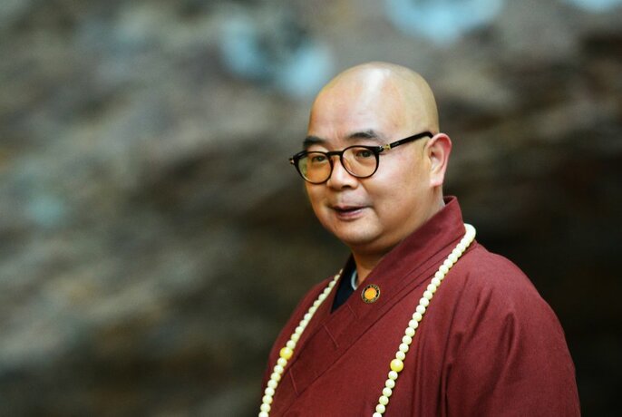 Artist Master Hong Si in a brown robe with a long white beaded necklace.