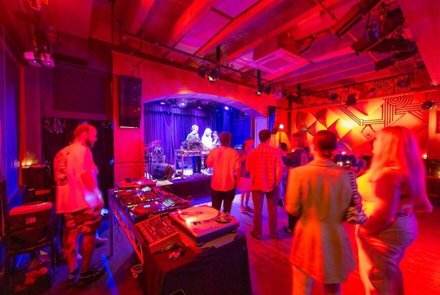People watching a gig in a small venue with bright red lighting.
