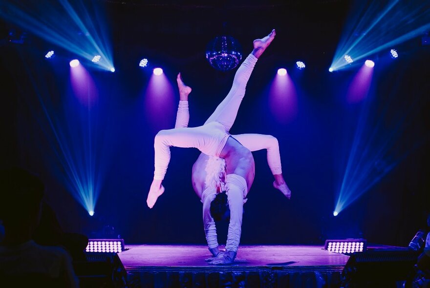 Two circus performers on stage in a handstand formation back to back.