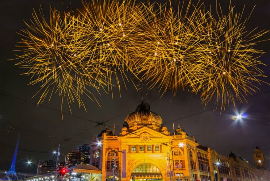 Fireworks exploding in the night sky above the facade of Flinders Street Station.