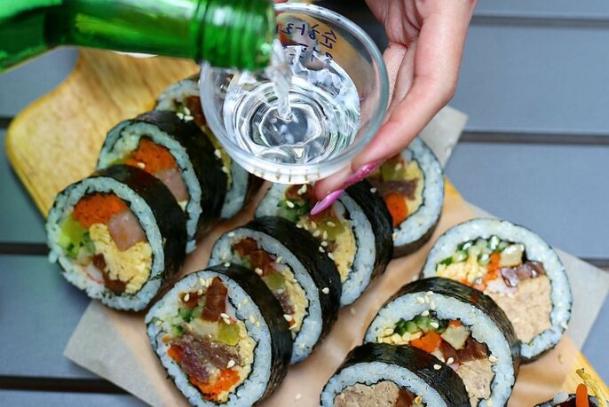 Spirit being poured into small glass over a platter of sushi rolls.