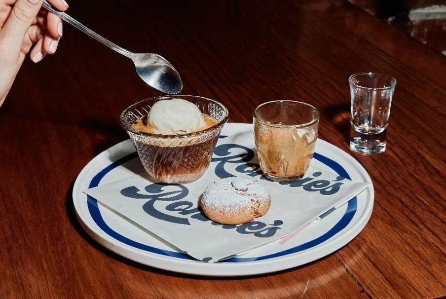 Affogato in a small glass bowl with a short black coffee glass and cookie on a plate with a 'Ronnie's' napkin; shot glass in the background.