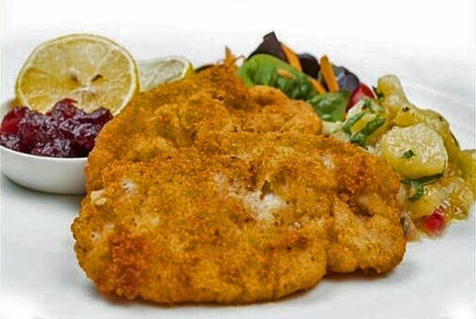 Schnitzel and vegetables with cranberry sauce and a slice of lemon.