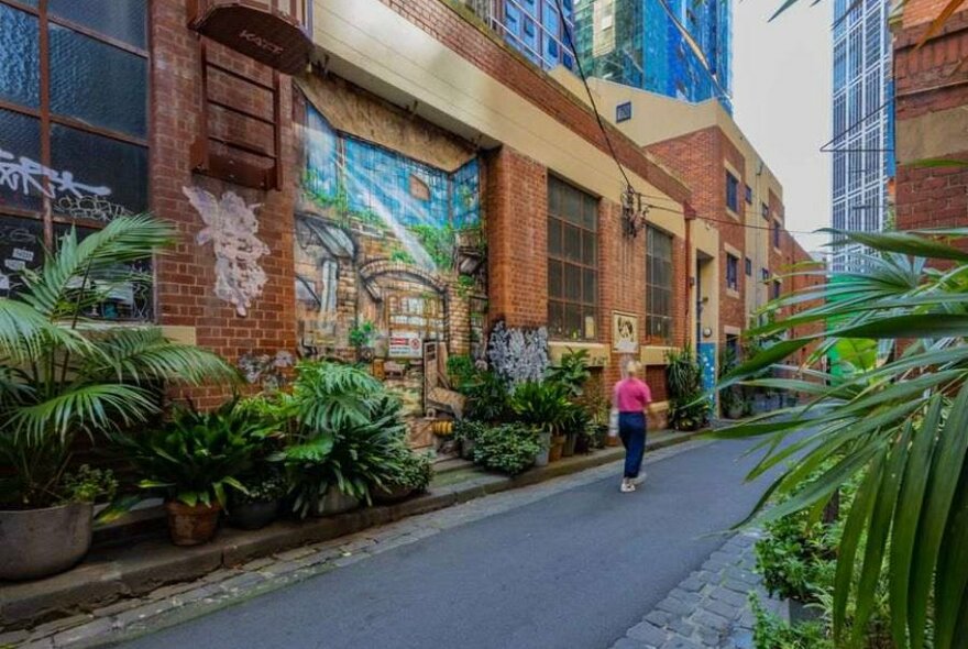 A woman in a pink jumper walking past a street art mural in a leafy laneway.