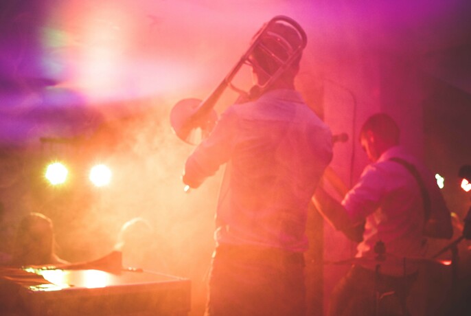 Trombone player and band playing on a stage with smoke and lights.