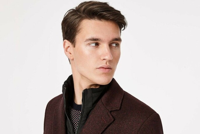 Model with head turned to look over his shoulder, wearing a purple jacket.