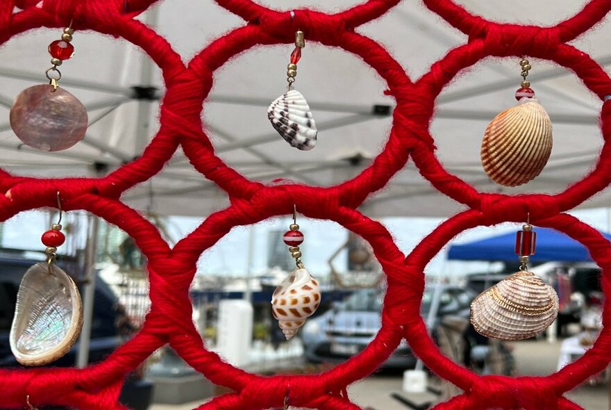 Looking through an handcrafted object made up of red rings and shells. 