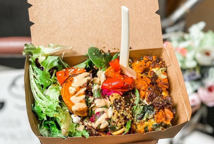 Cardboard takeaway container of salad and vegetables with plastic fork.