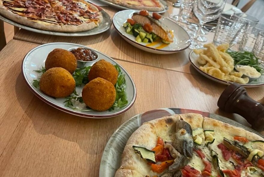 A table with many plates of Italian food including pizza, arancini and calamari.