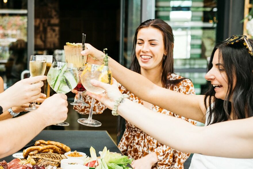 Group of people raising their glasses in a celebratory fashion over a table of food.