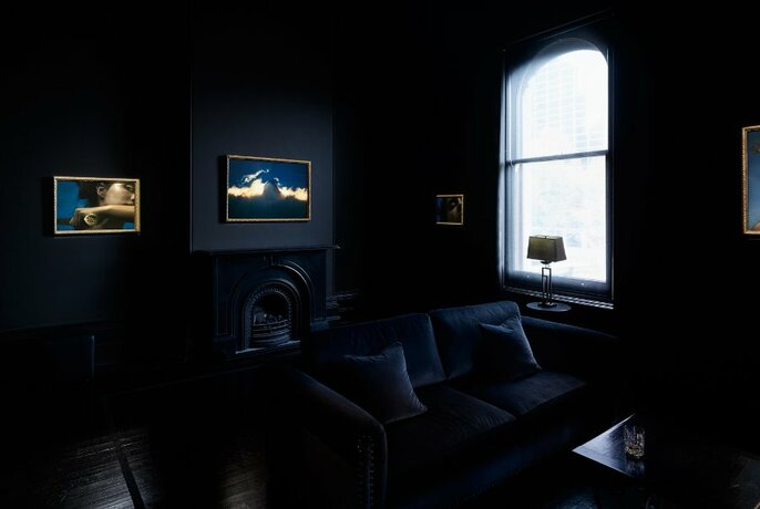 Dark room with artworks hanging on a wall, and a central couch and low table.