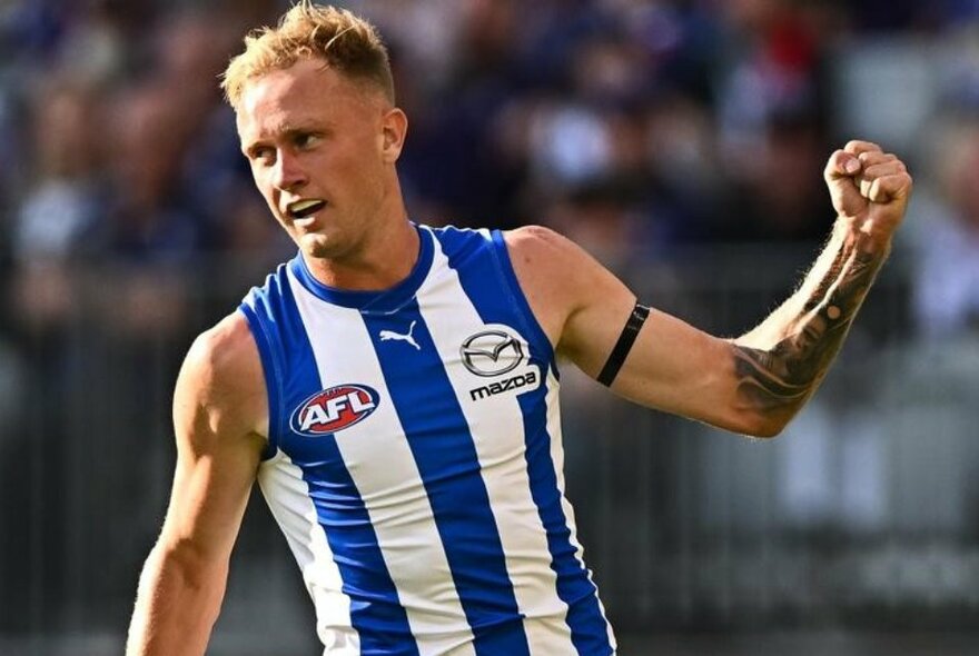 AFL player Jaidyn Stephenson wearing a North Melbourne jumper with his fist clenched, on the football field.