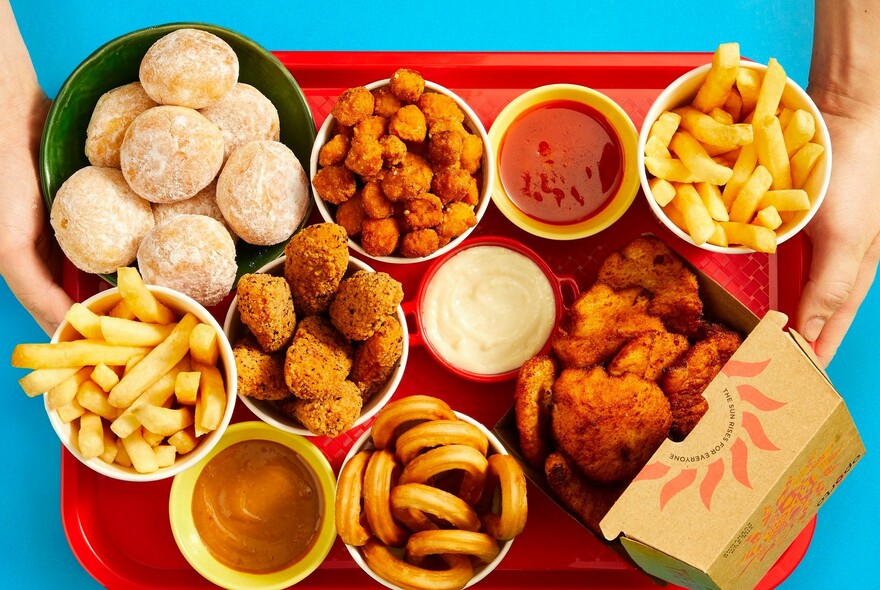 Red tray full of Oporto foods, including chips, nuggets, dipping sauces and donuts.