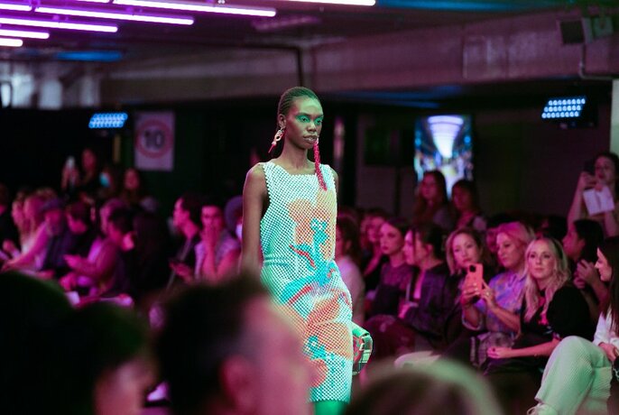 A model walks on a catwalk with people looking on. 