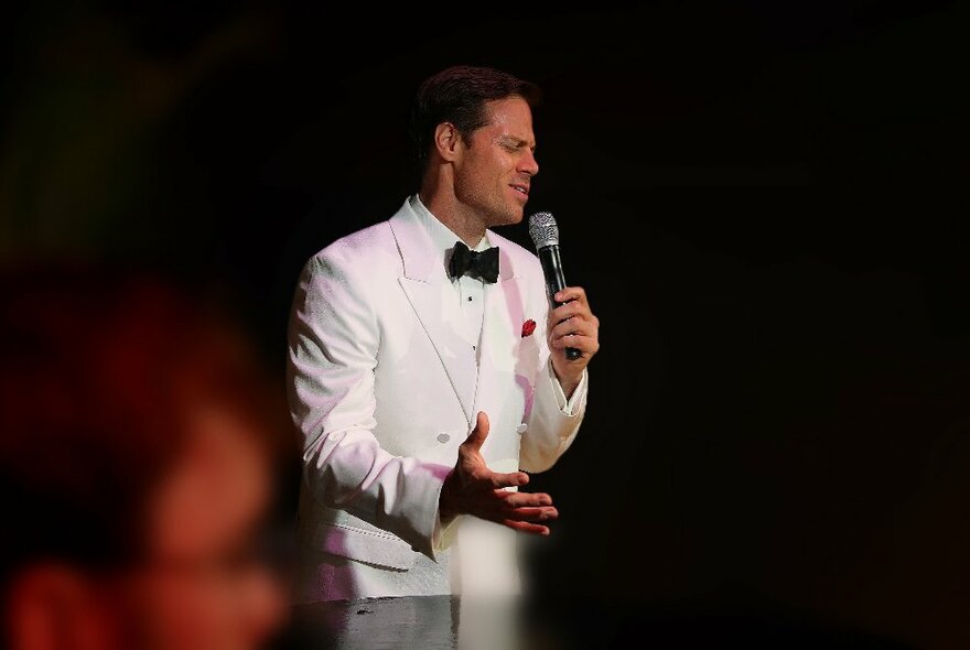 Performer, Mike Snell, singing on stage in a white tuxedo.