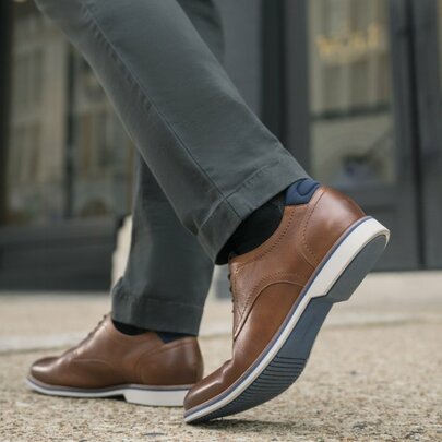 Brown leather shoes on a man wearing trousers, walking on pavement.