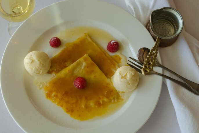 White plate of crepes suzette with cutlery.