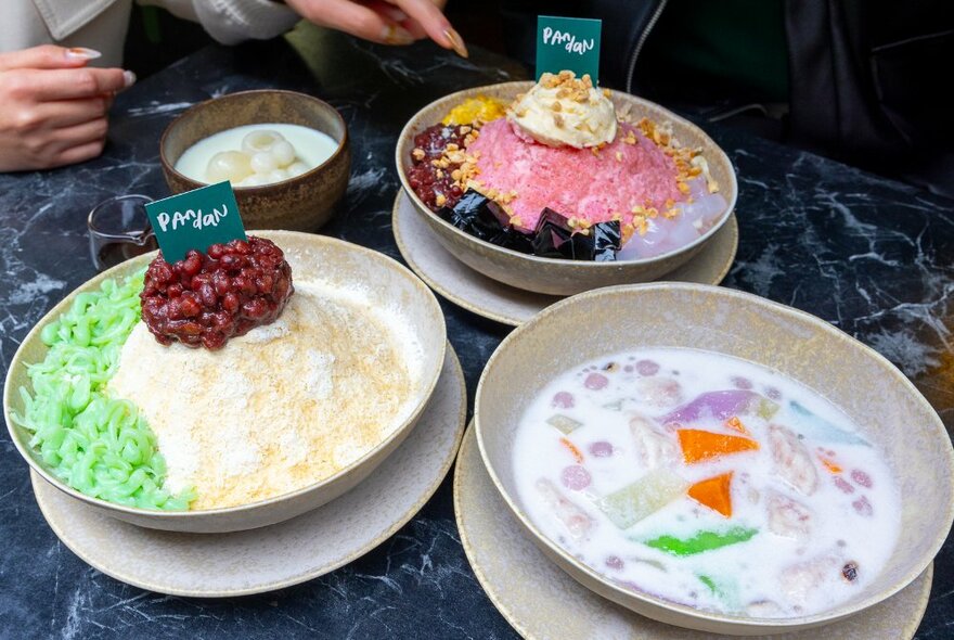 A selection of three colourful Malaysian desserts served in bowls on a table top.