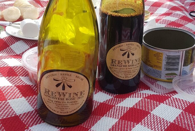 ReWine's refillable glass bottles on a red and white checked picnic rug with small plates of food also visible.