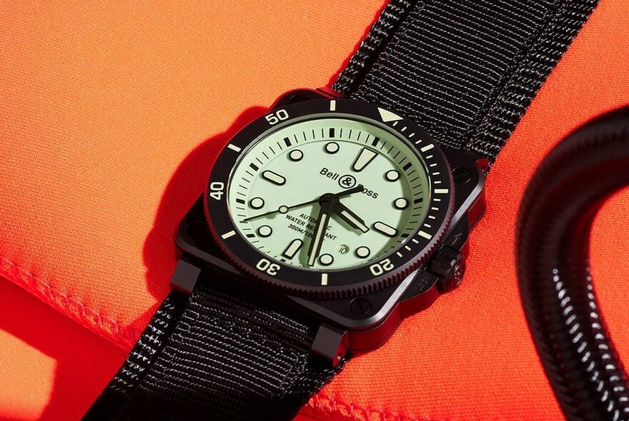 Men's chronometer-style watch on bright orange background, with luminous face and dial.
