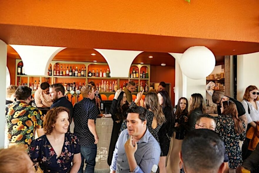 People at an outdoor bar with an orange roof and drinks area.