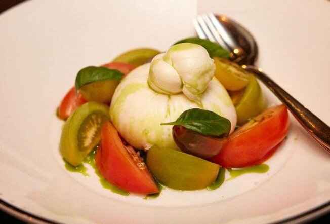 A ball of cheese on a plate of tomatoes.