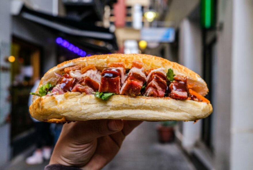 A banh mi held in front of a laneway.