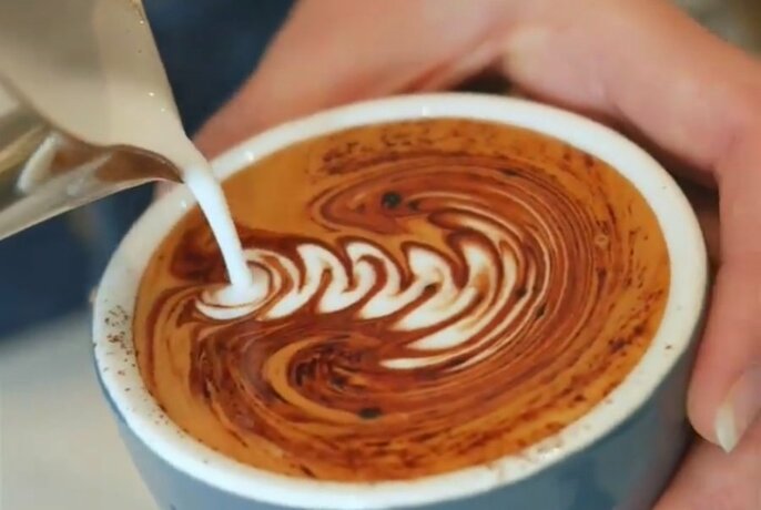 Milk being poured into a cup of coffee to create a pattern in the froth.