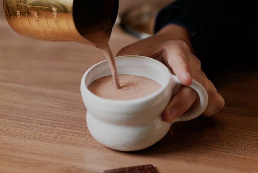 A person is pouring a hot chocolate into a mug
