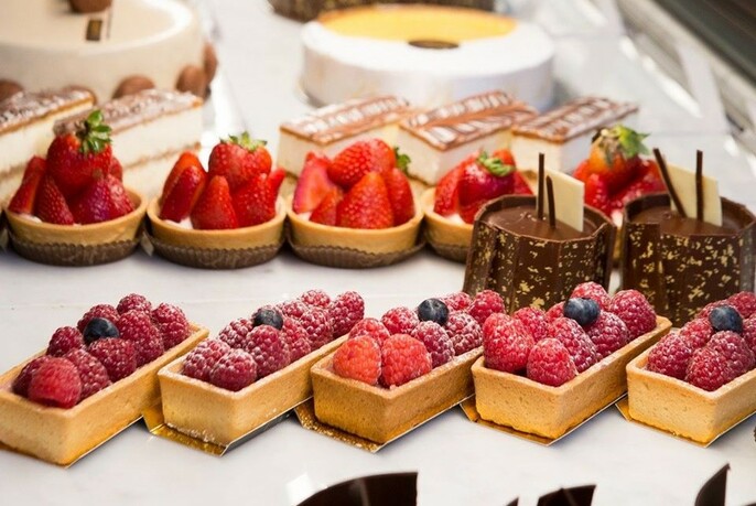 Three rows of pastries with cakes in background.