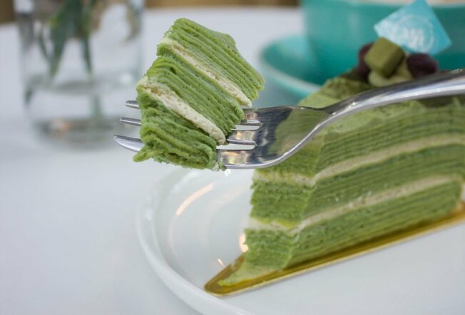 A fork cutting through a green multi-layer crepe cake.
