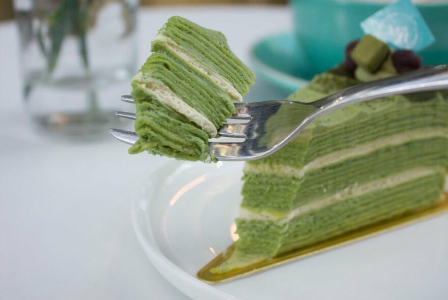 A fork cutting through a green multi-layer crepe cake.