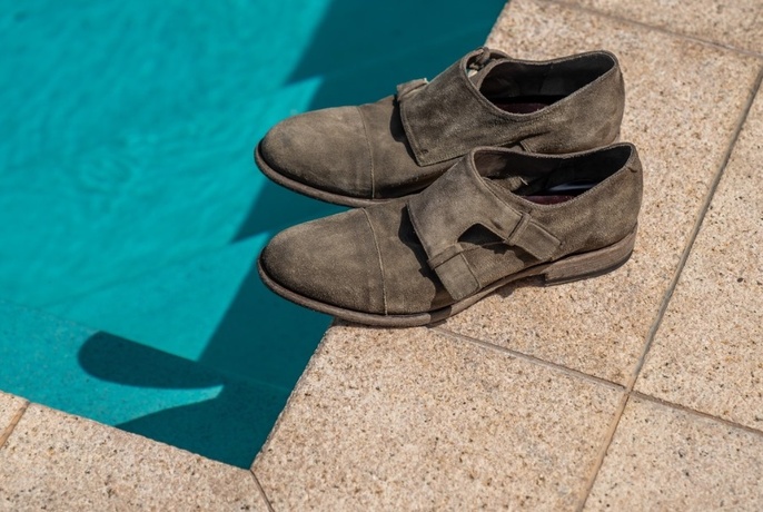 Dark grey suede shoes on edge of swimming pool.