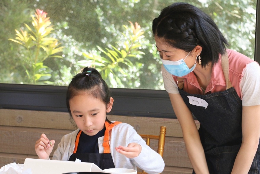 A teacher wearing a mask looks on while a child paints.
