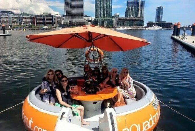 A round orange Aqua Donut boat with eight passengers shaded by the umbrella.