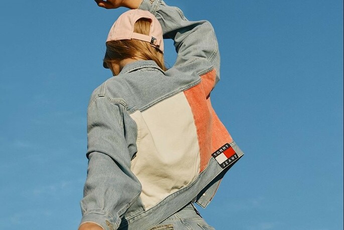 Back of model wearing a denim jacket with coloured panels, and pink cap.